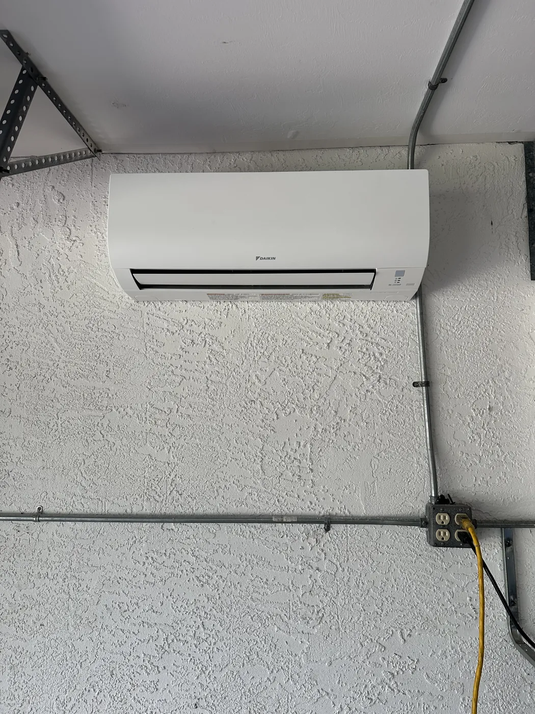A ductless indoor head mounted high on a wall, with the conduit and outlet serving it below